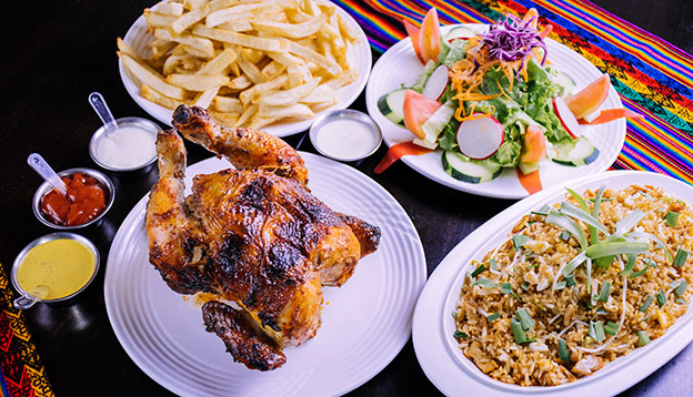pollo a la brasa - Peru roasted chicken served with salads and chips on a table