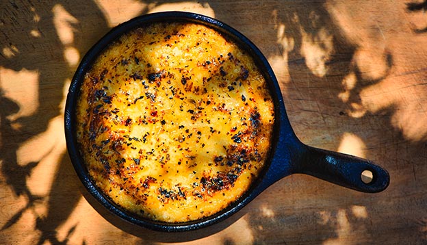 Delicious Argentinian Provolone Yarn Cheese (Provoleta) that was cooked in a cast iron skillet over the embers presented on an old wooden board