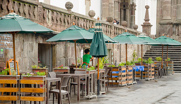 a restaurant with green huge umbrellas and chairs located in the historical centre of old town Quito