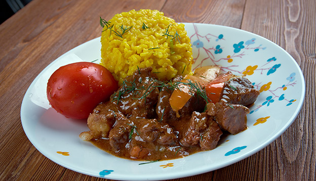 A plate of Seco, an Ecuadorian meta stew served with yellow rice and a tomato