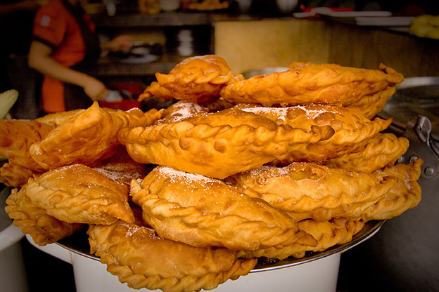 A tray of Empanadas de viento with a person cooking in the background