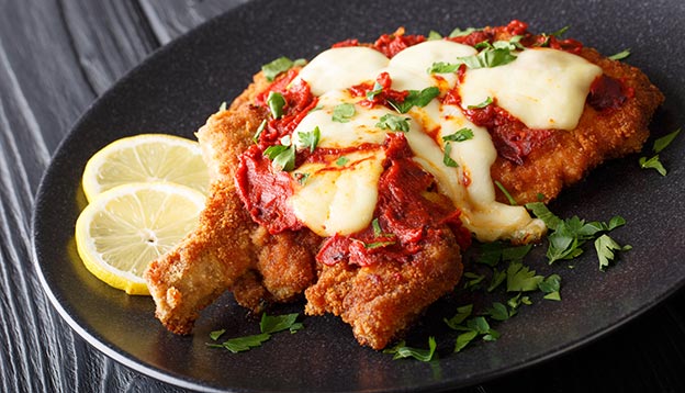 Milanesa napolitana Beef cutlet in breadcrumbs with mozzarella cheese and tomato sauce close-up on a plate. horizontal  A