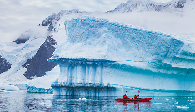2 people kayak alongside icebergs in Antarctica