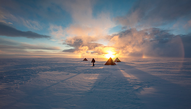 Antarctica Activities: People setting up tents with a sunset behind them.