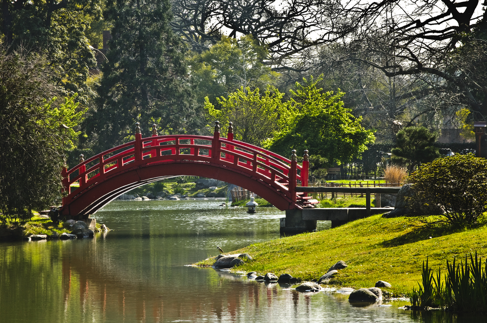 red japanese bridge over a pond with trees